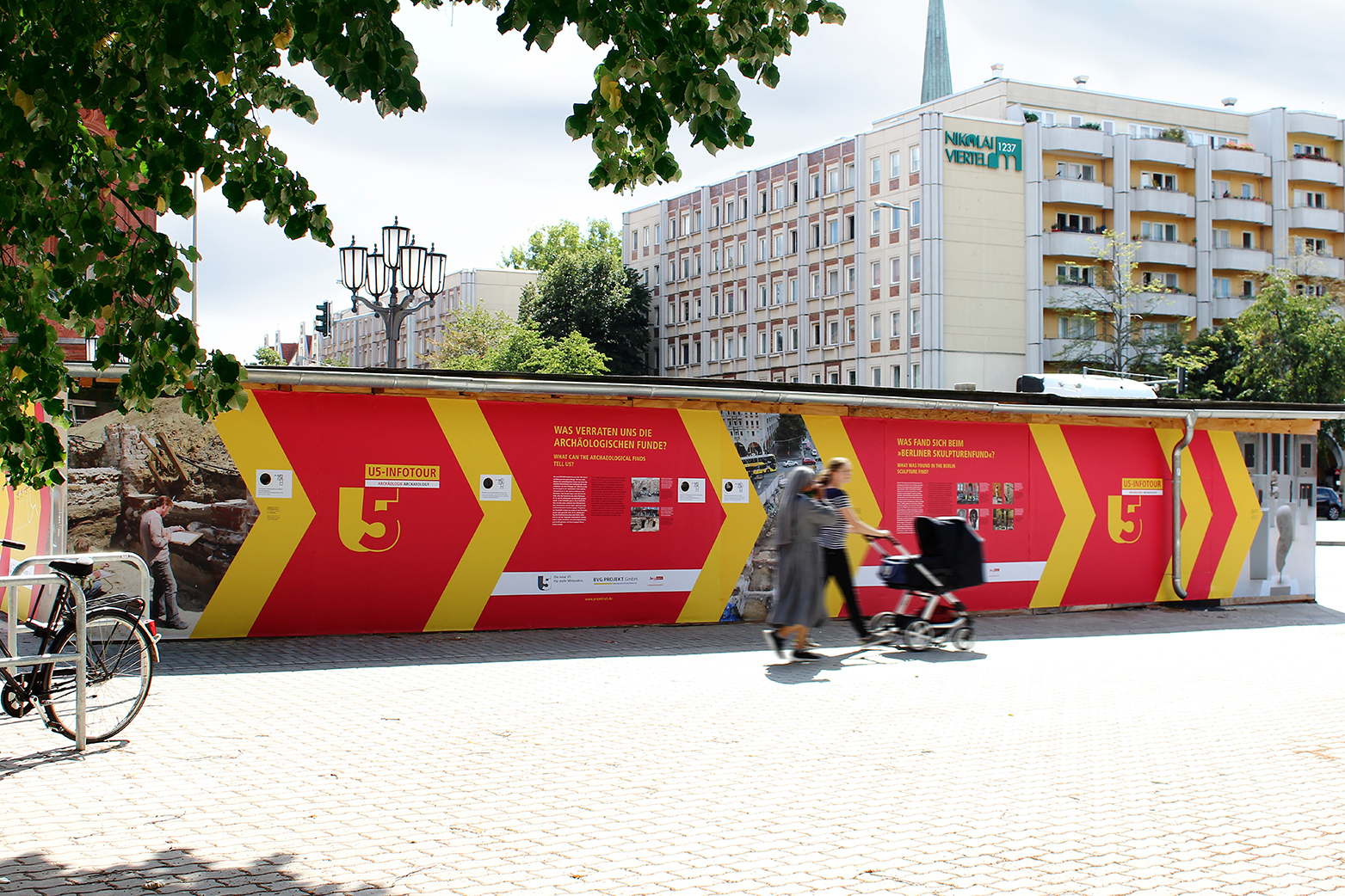 Outdoor Infotour mit gelb roter Wand zum Baufortschritt der u5 in Berlin Mitte.