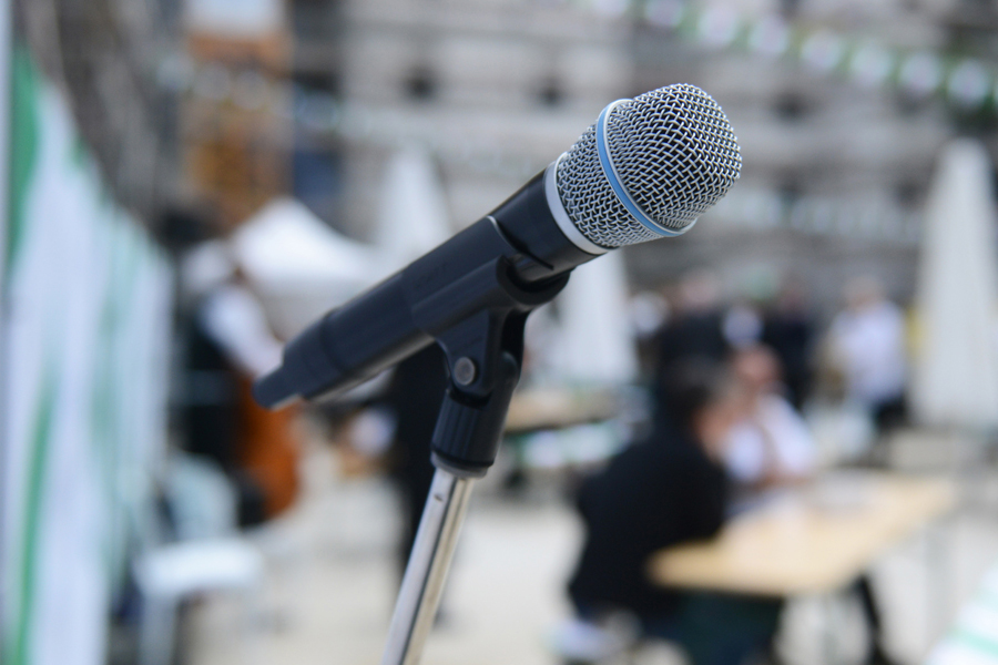 Ein Mikrofon mit verschwommenem Hintergrund, in dem Menschen zu erkennen sind.