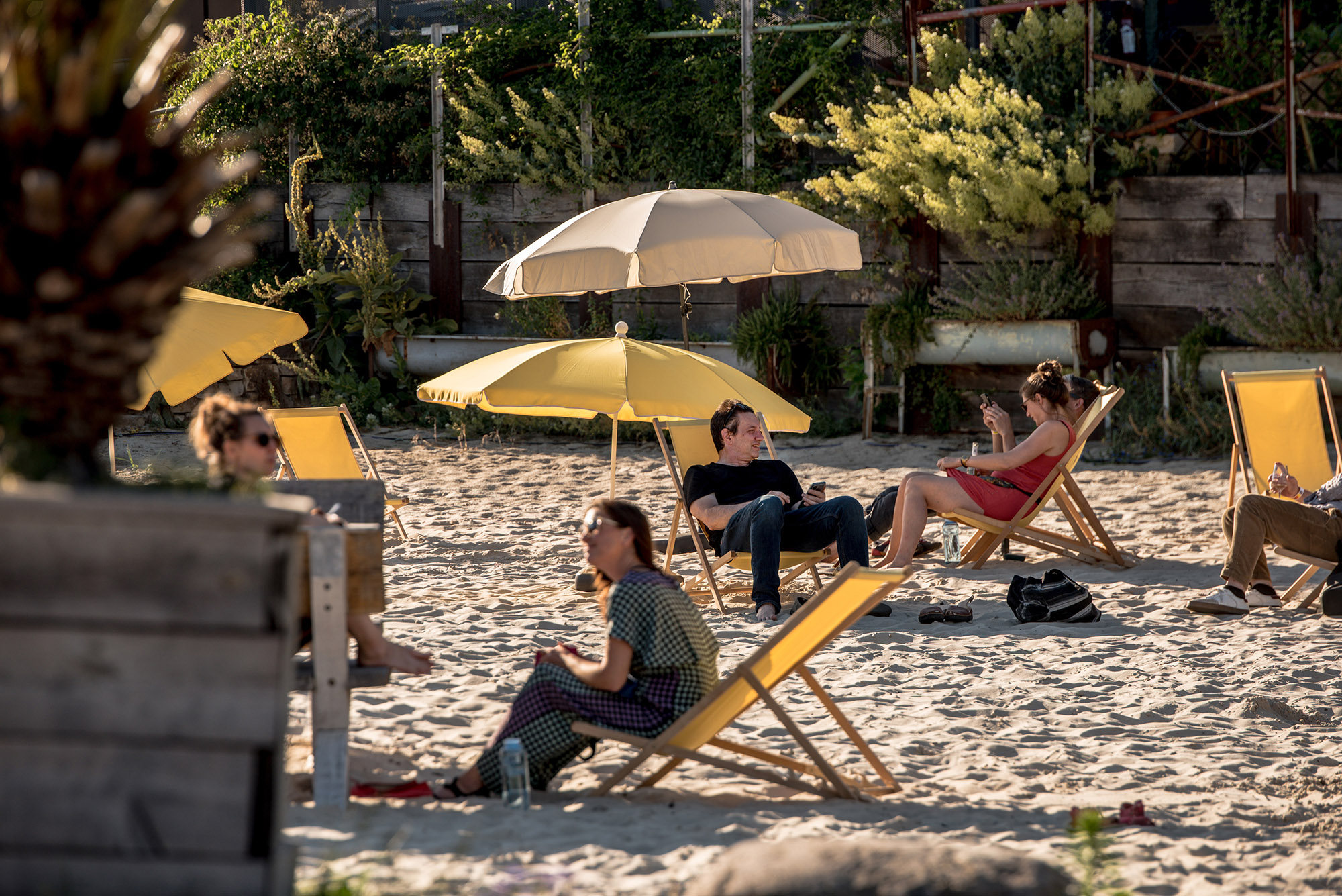 Sommerliche Stimmung auf dem Gelände der Malzfabrik – Menschen sitzen auf Stoffklappstühlen unter Sonnenschirmen am Stand.