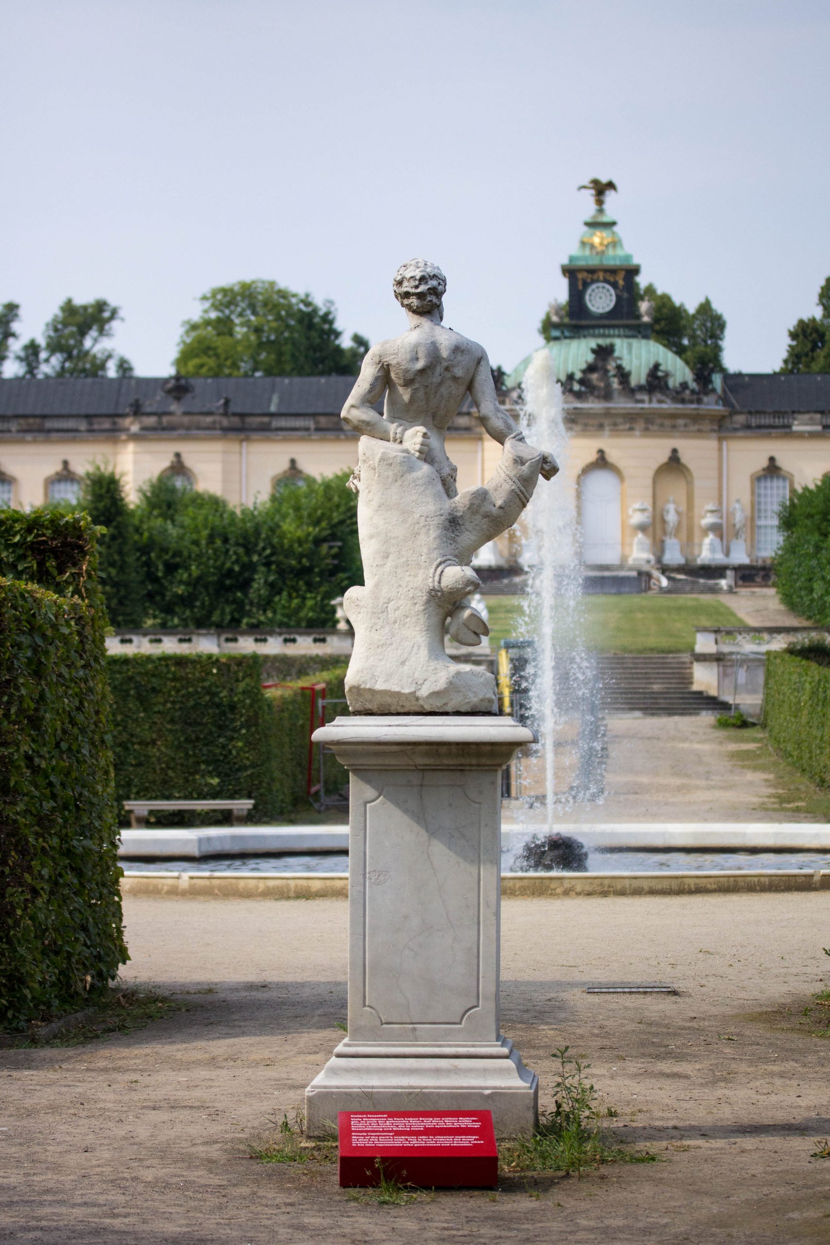 Eine Statue vor dem Schloss Sanssouci und einem roten Hinweisschild.