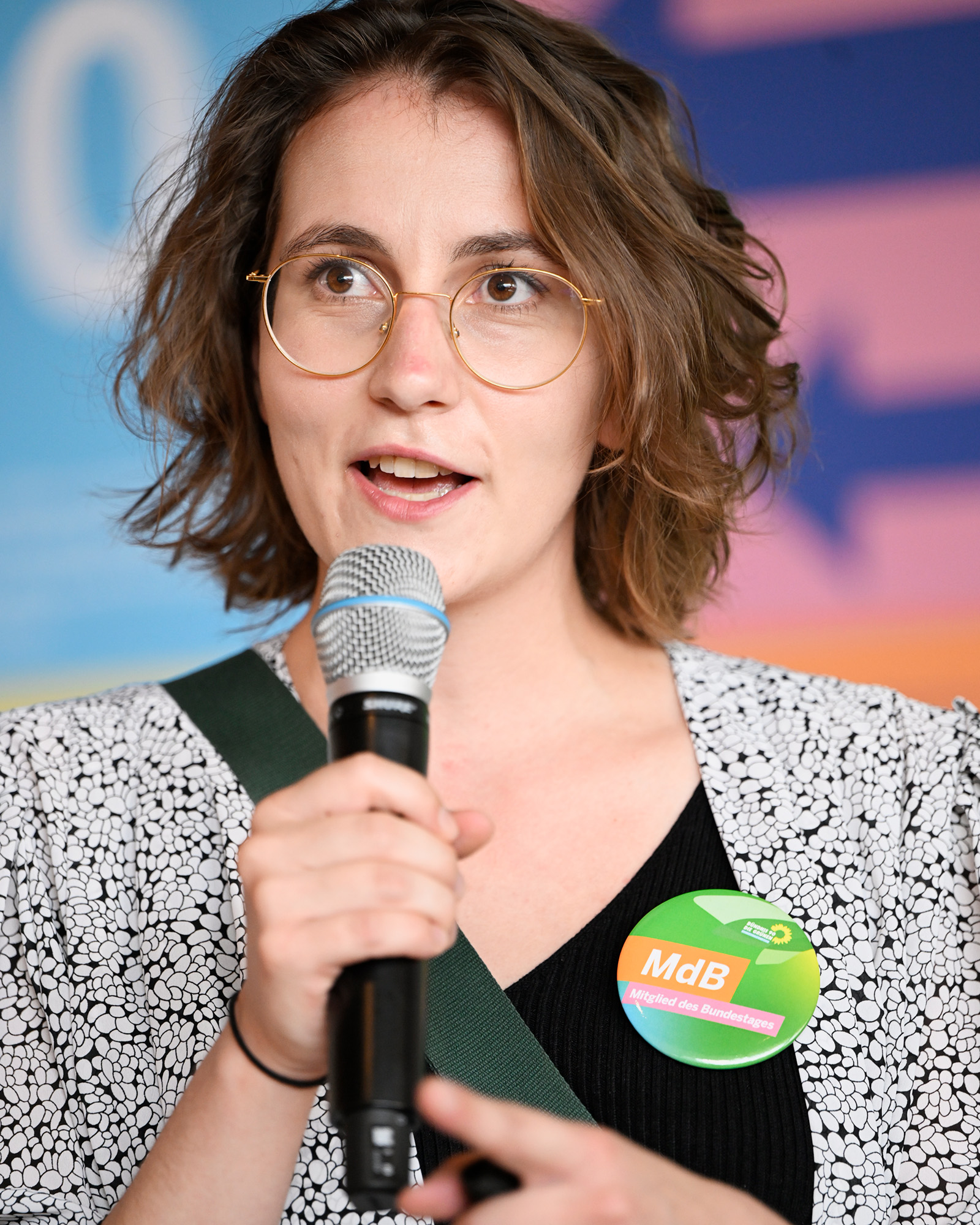 Eine junge Frau spricht in ein Mikrofon und trägt ein Button mit der Aufschrift: MdB Mitglied des Bundestages.